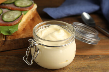 Obraz na płótnie Canvas Jar of delicious mayonnaise near fresh sandwich on wooden table