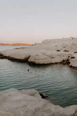The sandstone white rocks cliffs moonscape of Sarakiniki volcanic beach in Milos Island Greece surrounded by turquoise blue waves and sea at sunset
