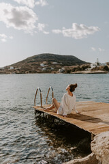 Young female traveller is relaxing at the deck by the sea in greece overlooking peaceful blue waves and sea and hills on the horizon on a sunny day