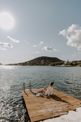 Young female traveller is relaxing at the deck by the sea in greece overlooking peaceful blue waves and sea and hills on the horizon on a sunny day