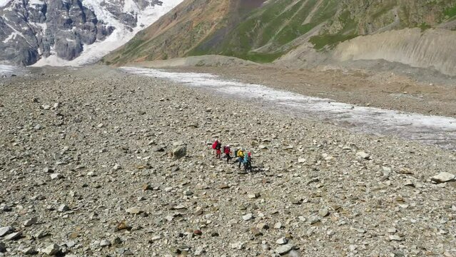 A group of tourists with backpacks hiking among the glacier moraine against the background of snowy mountain peaks