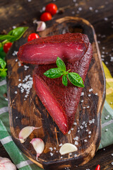 homemade jerky meat, basturma whole and in pieces, on a kitchen cutting board, dark and moody,...
