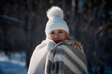 portrait of a young woman in the forest on a sunny winter day, a woman in a knitted hat and a warm plaid