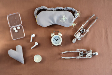 Concept of insomnia and nightmare disorder, flat lay. Sleeping mask, alarm clock and skeleton. Unhealthy sleep, disturbing and anxiety dreams. Top view