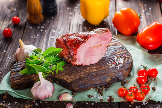 Meat balyk or boiled pork, beef and bacon, whole or piece cut on a kitchen cutting board, spices and vegetables, dark and moody, clouseup on a black wooden isolated background, top