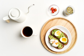 Flat lay avocado toast with eggs on dark bread, black coffee and glass of water on white background. High quality photo