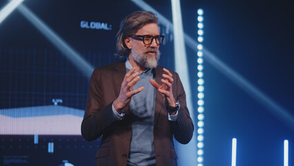 Male leader speaker presenter in casual clothes and glasses on stage gesturing and discussing the...