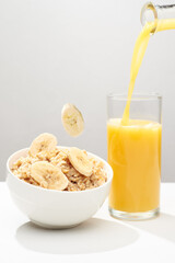 Oat porridge with levitating banana`s slices, walnut`s crumbs and glass of fresh orange juice on a white background.
