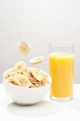 Oat porridge with levitating banana`s slices, walnut`s crumbs and glass of fresh orange juice on a white background.