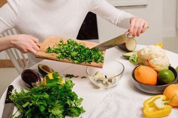 A young, beautiful vegetarian girl or blogger prepares breakfast of fruits, vegetables and greens at home in the kitchen. Blog about healthy eating
