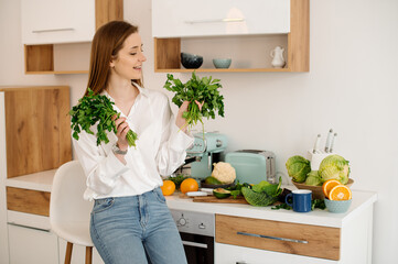 A young, beautiful vegetarian girl or blogger prepares breakfast of fruits, vegetables and greens at home in the kitchen. Blog about healthy eating