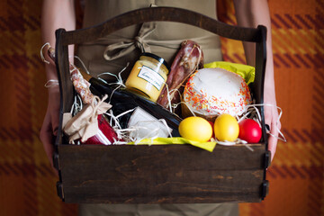 Female hands holding basket with colorful eggs, cake, red wine, hamon or jerky and dry smoked...