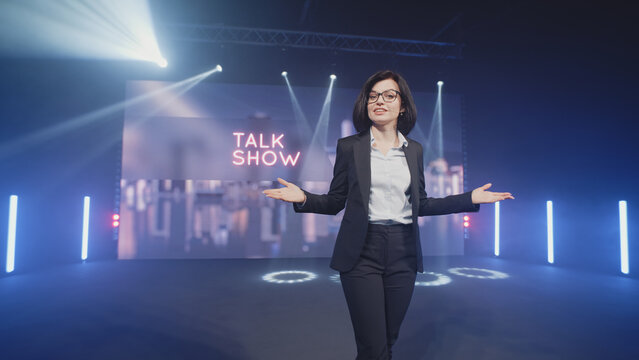 Happy presenter in a suit and glasses running onto the stage and announcing the start of the famous comedy, late-night show in an illuminated room with LED screen and 3D inscription