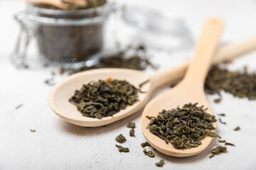Spoon of dried fragrant green tea leaves on a light cement background. Composition with organic, natural green tea. Copy space.
