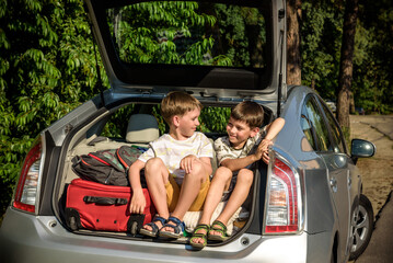 Two cute boys sitting in a car trunk before going on vacations with their parents. Two kids looking forward for a road trip or travel. Summer break at school. Family travel by car