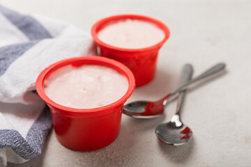 strawberry yogurt in a red plastic cup with a spoon on a white background.