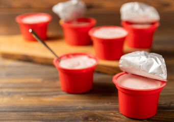 strawberry yogurt in a red plastic cup with a spoon on a dark wooden background.