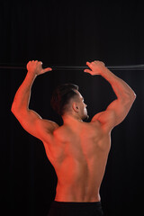 back view of shirtless sportsman exercising on horizontal bar isolated on black.