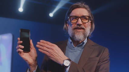 Presenter standing on stage with a new contemporary smartphone at the presentation, and explaining...