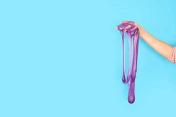 Close up on shiny purple or violet slime in the hand isolated on blue background. Fun and stress relief concept. Banner with copy space.