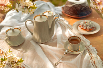 Coffee set on a white tablecloth on a sunny day, cherry blossom, cupcake, pudding. Outdoor, picnic,...