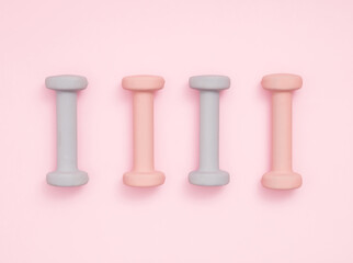 Four pastel color exercise weights on pastel pink background with soft shadow. Exercise, healty lifestyle or New Year resolution concept. Flat lay.