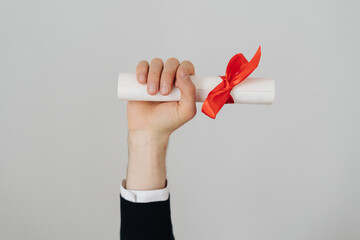 Male hand hold graduation bachelor diploma with a red bow on white background