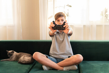 Teenager boy is playing on the console, video games, child with video game joystick. Gamepad playing video , enjoying weekend at home, kids entertaining concept, spending time in living room at home.