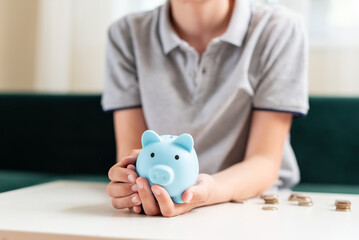 Obraz na płótnie Canvas Kid teen boy saving money putting coins in a piggy bank. Learning financial responsibility and projecting savings. The concept of saving money, finance, business and investment, Lessons in mindfulness