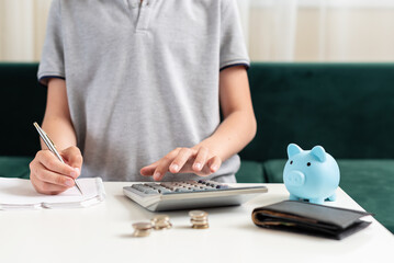 Fototapeta na wymiar Kid teen boy counting money and taking notes, saving money in a piggy bank. Learning financial responsibility and projecting savings. Concept of finance, business, investment. Lessons in mindfulness