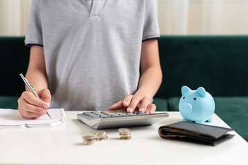 Fototapeta premium Kid teen boy counting money and taking notes, saving money in a piggy bank. Learning financial responsibility and projecting savings. Concept of finance, business, investment. Lessons in mindfulness