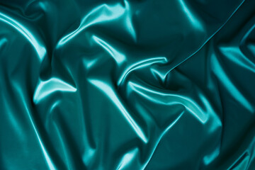 Photography of beautiful wavy turquoise silk satin luxury cloth fabric with monochrome background design. 
