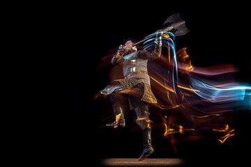 Dynamic portrait of brutal serious man, medieval knight with swinging ax fighting isolated over dark background in neon mixed light. Art, history, creativity