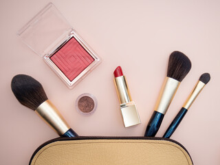 Top view of cosmetics standing out from beige makeup bag on pink background