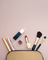 Top view of cosmetics standing out from beige makeup bag on pink background