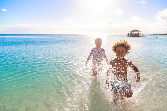 A Cute diverse boy and little girl running and splashing together in the Caribbean ocean in the late afternoon while on a family vacation