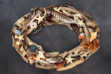 Driftwood, seashell, feather and seaweed oval shaped wreath on grunge grey background. Natural...