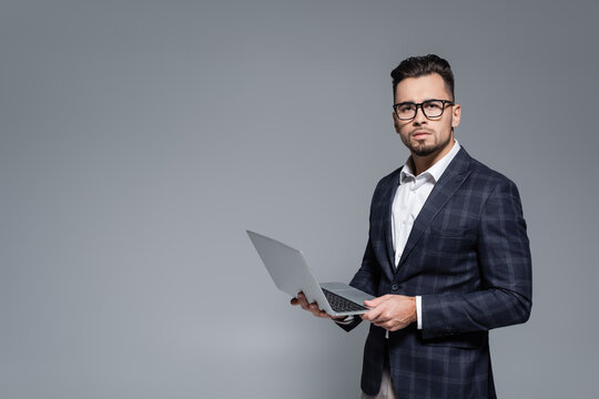businessman in suit and glasses holding laptop isolated on grey.