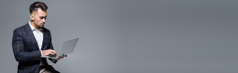 bearded businessman in suit using laptop isolated on grey, banner.