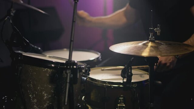 A young attractive male drummer plays with sticks on a drum kit. Makes hits on metal cymbals or Crash. Home rehearsal studio for recording sound and songs. Plays rock or heavy metal music.