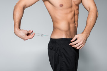 cropped view of shirtless and muscular sportsman injecting himself with steroids on grey.