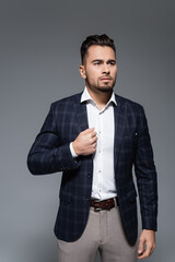 bearded businessman adjusting plaid blazer isolated on grey.