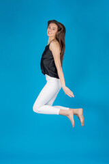 Leisure concept. Beautiful brunette slim woman with long hairs jumps in air on blue background with...