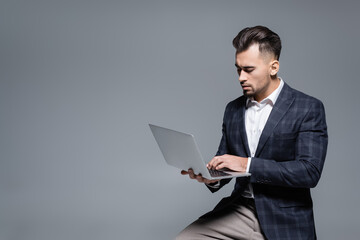 bearded businessman in suit using laptop isolated on grey.