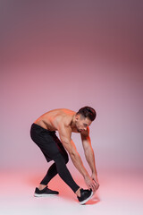 shirtless sportsman leaning while stretching on grey and pink.