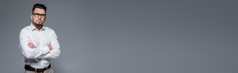 bearded businessman in white shirt and glasses standing with crossed arms isolated on grey, banner.