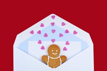 Smiling gingerbread man in an envelope with a letter and many sweet hearts, red background. The...