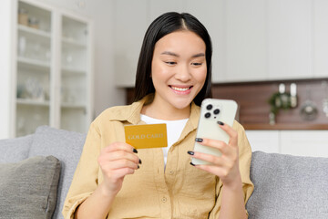 Cheerful young asian woman using smartphone shopping app for buying online, holding credit card and...