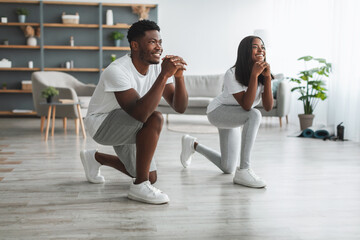 Happy African American couple doing forward lunges at home