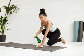 Sport Equipment Disinfection. Young Beautiful Woman Applying Sanitizer Spray On Yoga Mat